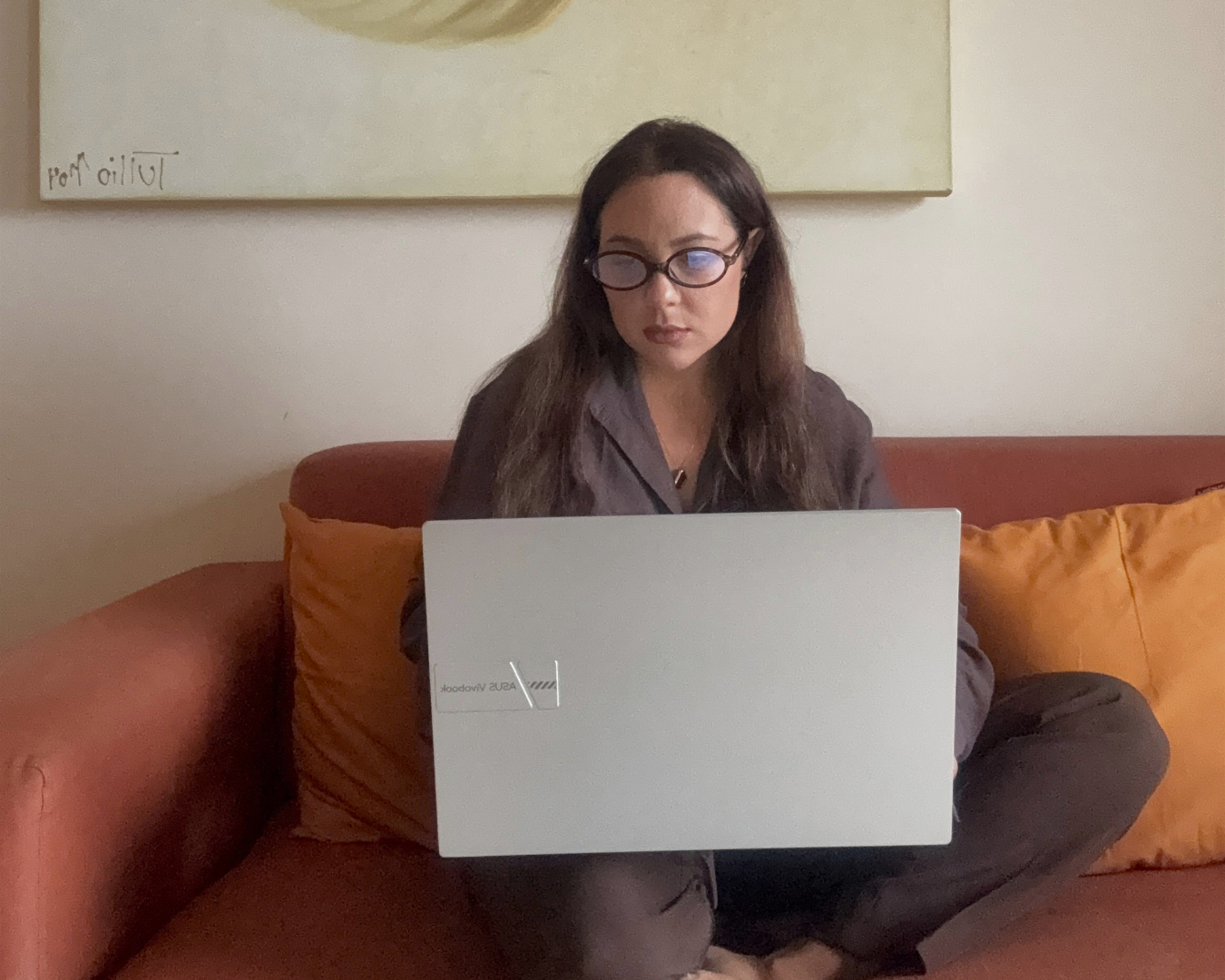 Estrategista ÂMIA trabalhando no notebook deitada em um sofá com almofadas laranja